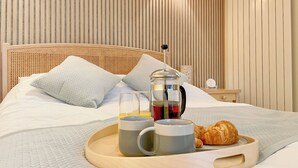Un lit bien fait, avec des oreillers, une tablette sur laquelle se trouvent une cafetière, une tasse et un croissant.