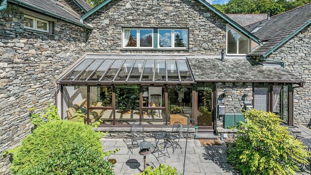 Une maison en pierre dotée d’une véranda en verre, d’un espace extérieur aménagé pour s’asseoir et d’un chemin en pierre.