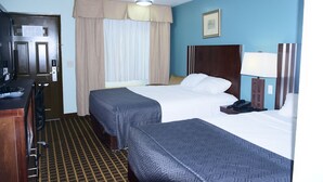 Habitación de hotel con dos camas, un escritorio, teléfono, lámpara y ventana con cortinas.