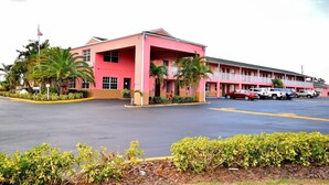 Un motel rosa con área de estacionamiento techada y varios coches estacionados al frente.
