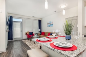 A modern kitchen with granite countertops, red placemats, and a dining area with a red chair and a small table.