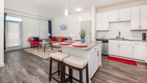 A modern kitchen with white cabinets, a central island with stools, and a dining area with a red rug. - Luxury Apt | Work from here | King Bed | Fast WiFi |6mi to CLT✈️ (Charlotte)
