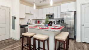 A modern kitchen with white cabinets, stainless steel appliances, and a central island with stools. - Luxury Apt | Work from here | King Bed | Fast WiFi |6mi to CLT✈️ (Charlotte)