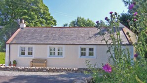 A single-story house with a sloped roof, a stone wall in front, and a bench outside. - Single storey cottage for 4/6 in Twynholm only 3 miles from Kirkcudbright. (Twynholm by Kirkcudbright)