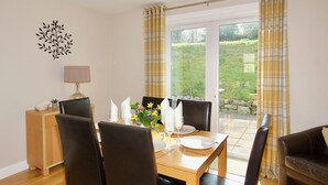 A dining area with a wooden table set for four, surrounded by black chairs. A small side table with a lamp and a bowl of fruit is visible. - Single storey cottage for 4/6 in Twynholm only 3 miles from Kirkcudbright. (Twynholm by Kirkcudbright)