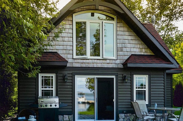 A two-story house with a large bay window, a sliding glass door, and a barbecue grill outside.