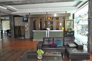 A modern lobby with a reception desk, leather sofas, a coffee table with a plant, and a large window offering a view of the street.