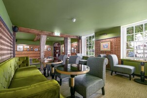 A cozy room with green walls, patterned wallpaper, and a green sofa. There are several patterned armchairs and a round table with chairs.