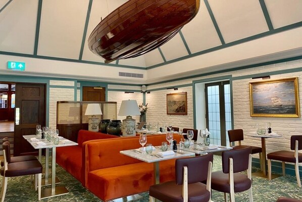A restaurant with booths and tables, a wooden ceiling, and a painting on the wall. - Red Lion Hotel (Henley-on-Thames)