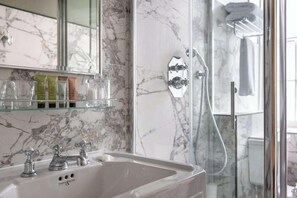 A bathroom with a marble sink, a glass shower enclosure, and a mirror above the sink.
