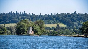Una propiedad junto al lago con una estructura tipo pabellón rodeada de abundante vegetación y colinas al fondo.