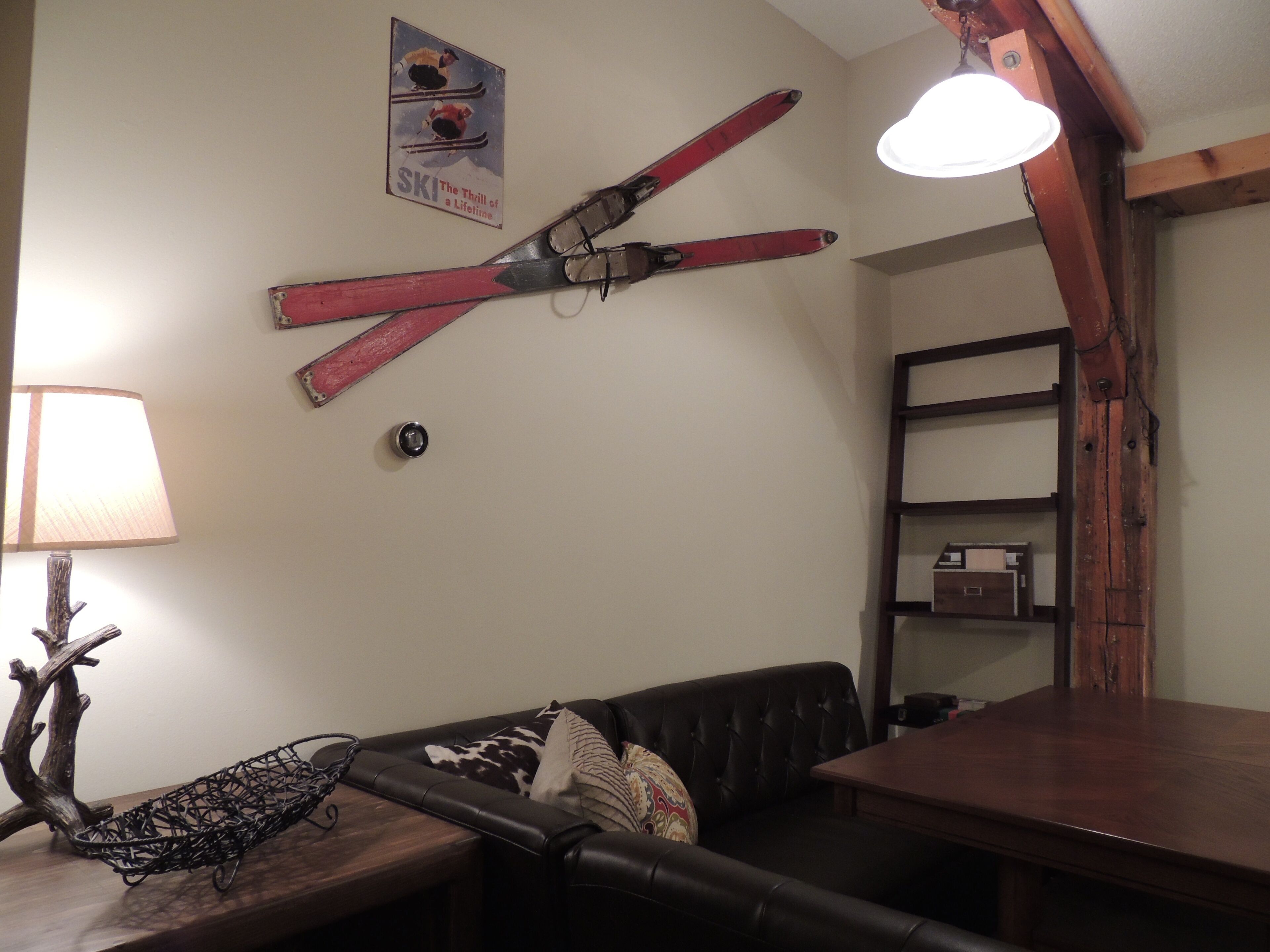 A cozy living room with a wooden table, a leather sofa, and a wall-mounted ski rack.