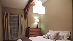 A bedroom with a bed, a nightstand, a lamp, and a window with curtains. - Best Location! Renovated center village Okemo 2 BR - free shuttle outside door! (Ludlow)