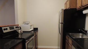 A compact kitchen with wooden cabinets, a stainless steel refrigerator, a microwave, and a stove. - Best Location! Renovated center village Okemo 2 BR - free shuttle outside door! (Ludlow)