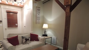 A cozy living room with a white sofa, red cushions, a wooden coffee table, and a lamp. - Best Location! Renovated center village Okemo 2 BR - free shuttle outside door! (Ludlow)
