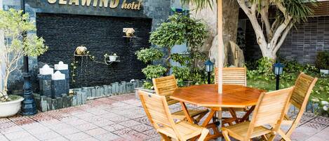 A SEA WIND hotel outdoor seating area with a stone wall, potted plants, and a wooden table with chairs.