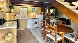 A compact kitchen with wooden cabinets, a washing machine, and a dining area with a table and chairs. - 3 bedroom accommodation in Leintwardine, near Ludlow (Leintwardine, near Ludlow)