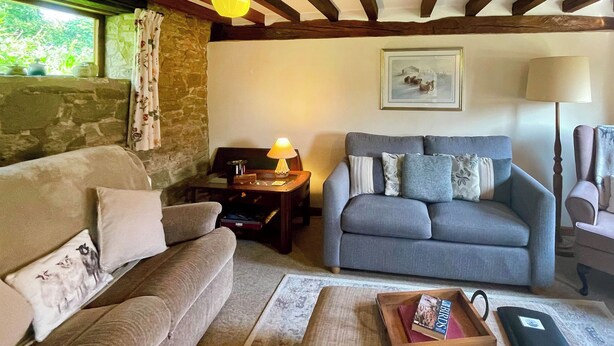 A cozy living room with a grey sofa, a wooden coffee table, and a lamp. There's a stone wall and a window with curtains. - 3 bedroom accommodation in Leintwardine, near Ludlow (Leintwardine, near Ludlow)