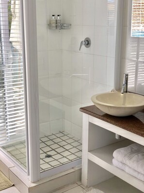 A bathroom with a glass shower enclosure, a sink with a marble countertop, and a towel rack.
