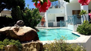 Ein Schwimmbecken mit einem weißen Gebäude im Hintergrund, umgeben von Grünpflanzen und Felsen.