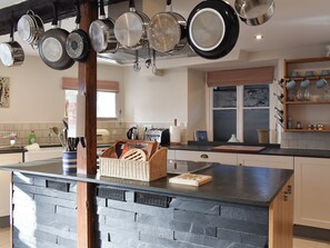 A kitchen with a central island, hanging pots, and a variety of utensils.