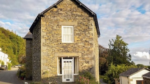 Une maison en pierre avec deux fenêtres, un petit porche et un jardin.