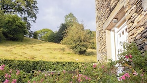 Un bâtiment en pierre, avec une clôture en bois et des fleurs roses au premier plan.