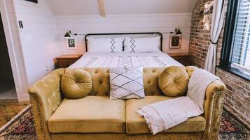 A bedroom with a bed, a gold-colored sofa, and a brick wall.