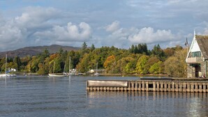 A calm lake with boats, a wooden dock, and a stone building with a pointed roof. - Pine Rigg - Quarry Rigg (Bowness-on-Windermere)