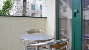 A small outdoor table and chair set against a building wall, with a glass door and window in the background. - Pine Rigg - Quarry Rigg (Bowness-on-Windermere)