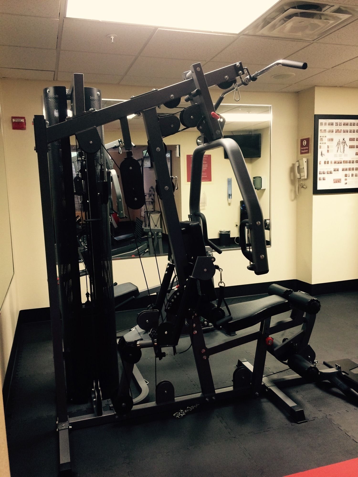 A gym with a weight machine, a mirror, and a poster on the wall.