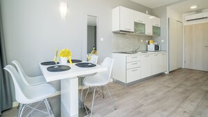 A modern kitchen with white cabinetry, a dining area with a white table and chairs, and a visible microwave. - Apartments Zoom Zoom-Studio Apartment with Balcony (Grey) (Dubrovnik)