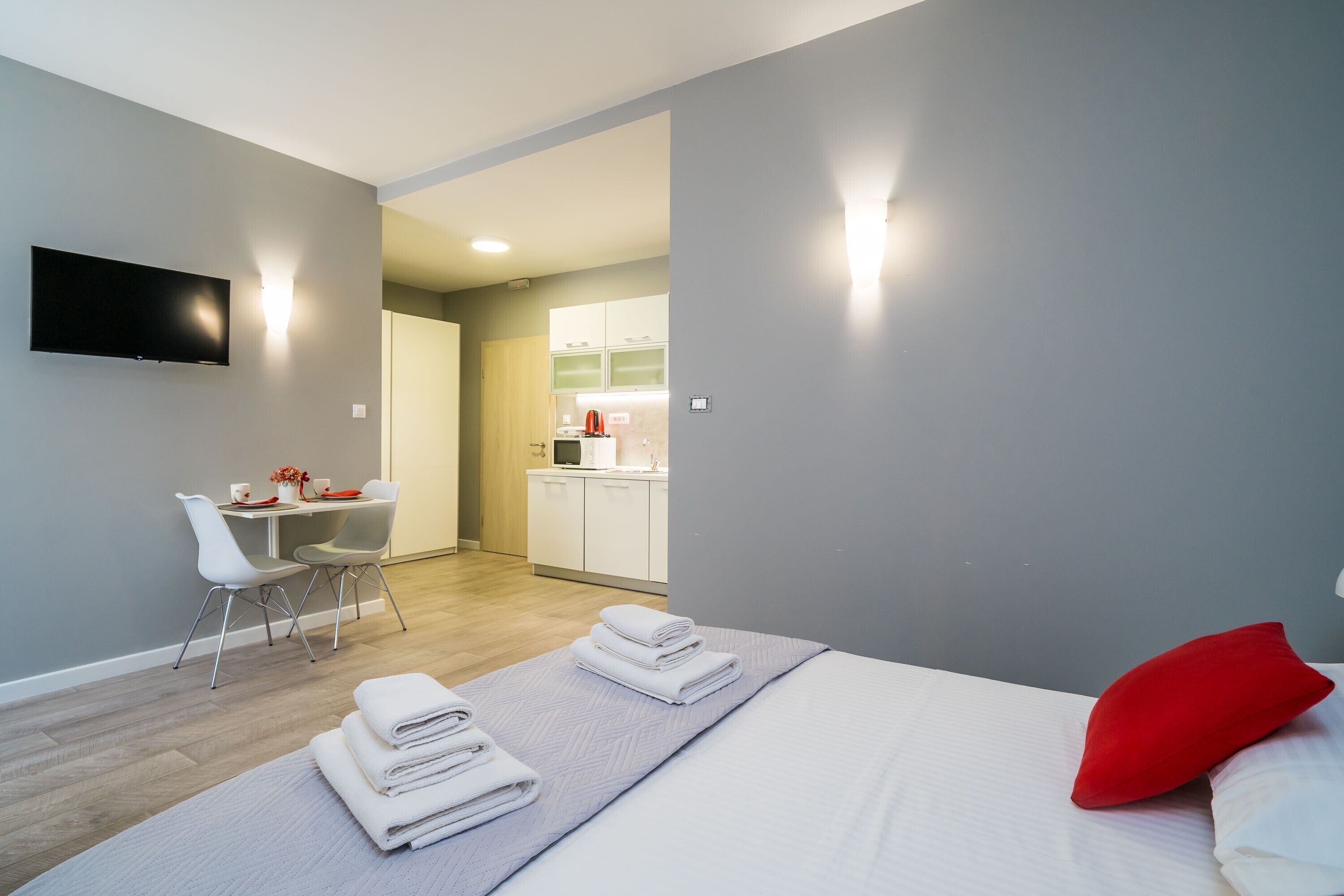 A modern hotel room with a bed, a desk, and a kitchenette.