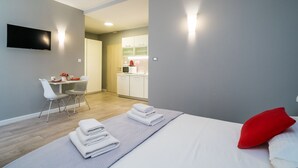 A modern hotel room with a bed, a desk, and a kitchenette.