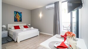 A modern hotel room with a neatly made bed, a dining table set for two, and a large window with curtains.