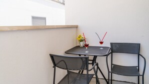 A small outdoor seating area with two metal chairs and a table, a vase with yellow flowers, and two glasses of red wine with red straws.