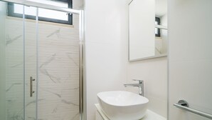 A modern bathroom with a glass shower enclosure, a white sink with a vessel basin, and a large mirror.