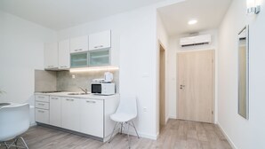 Una cocina moderna con armarios blancos, un microondas y una cafetera. Se observa una silla blanca y una puerta de madera al fondo.
