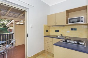 Cocina compacta con microondas, estufa y un lavamanos pequeño. Una silla y una mesa están afuera de la puerta.