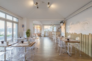 A spacious cafe with clear plastic chairs and wooden tables, large windows offering views of the city, and a wooden fence along one wall.