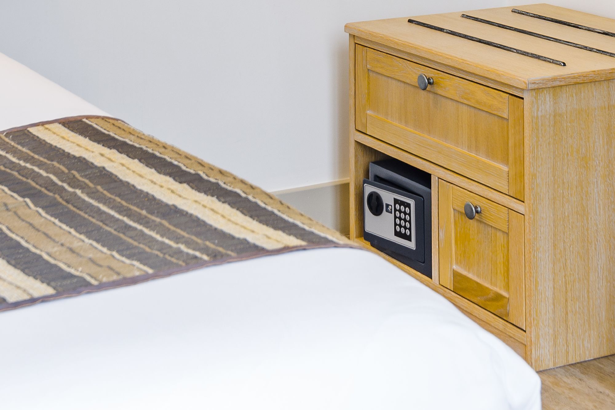Una cama con un edredón a rayas, una mesita de noche de madera con caja fuerte integrada y un aparador de madera con espejo.