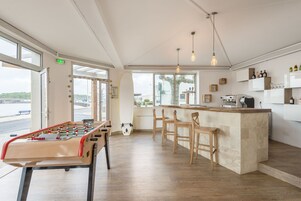 A modern kitchen with a bar area, wooden stools, and a foosball table.