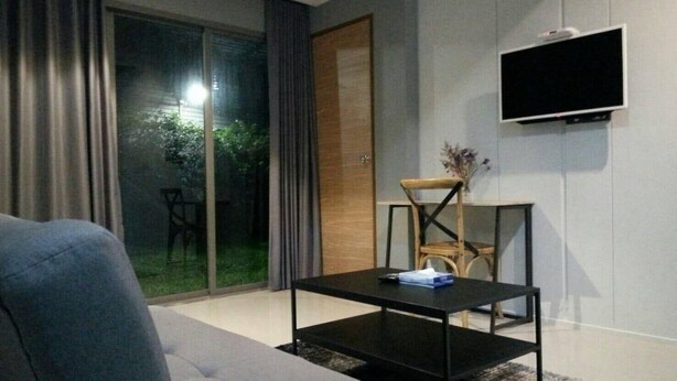 Una sala de estar moderna con un sofá, una mesa de centro, un televisor montado en la pared y un ventanal corredero que da a un espacio exterior.