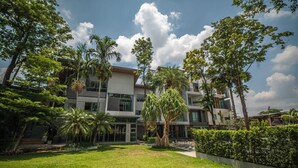 Un edificio moderno de varios pisos con un césped cuidado y diversas especies de árboles.