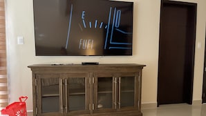 A modern living room with a large flat-screen TV mounted on the wall, a wooden cabinet below, and a closed door to the right. - Pool and close to ocean (Túxpam de Rodríguez Cano)
