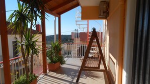 A balcony with potted plants, a wooden swing, and a view of the surrounding buildings. - Oasis Studios (Kefalonia)
