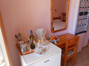 A compact room with a white desk, a small refrigerator, a mirror, and a wooden chair. - Oasis Studios (Kefalonia)
