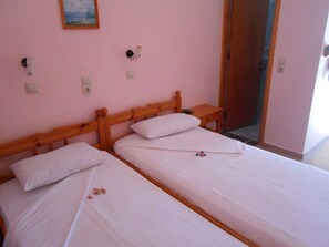A room with two single beds, a wooden headboard, a small bedside table with a remote control, and a wall-mounted light fixture. - Oasis Studios (Kefalonia)