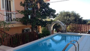 A rectangular swimming pool with a stone archway, surrounded by a tiled deck and a wooden fence. - Oasis Studios (Kefalonia)