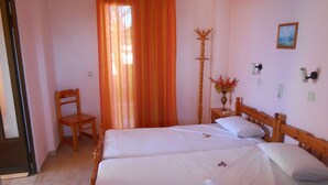 A bedroom with two beds, a wooden chair, a coat rack, and a painting on the wall. - Oasis Studios (Kefalonia)